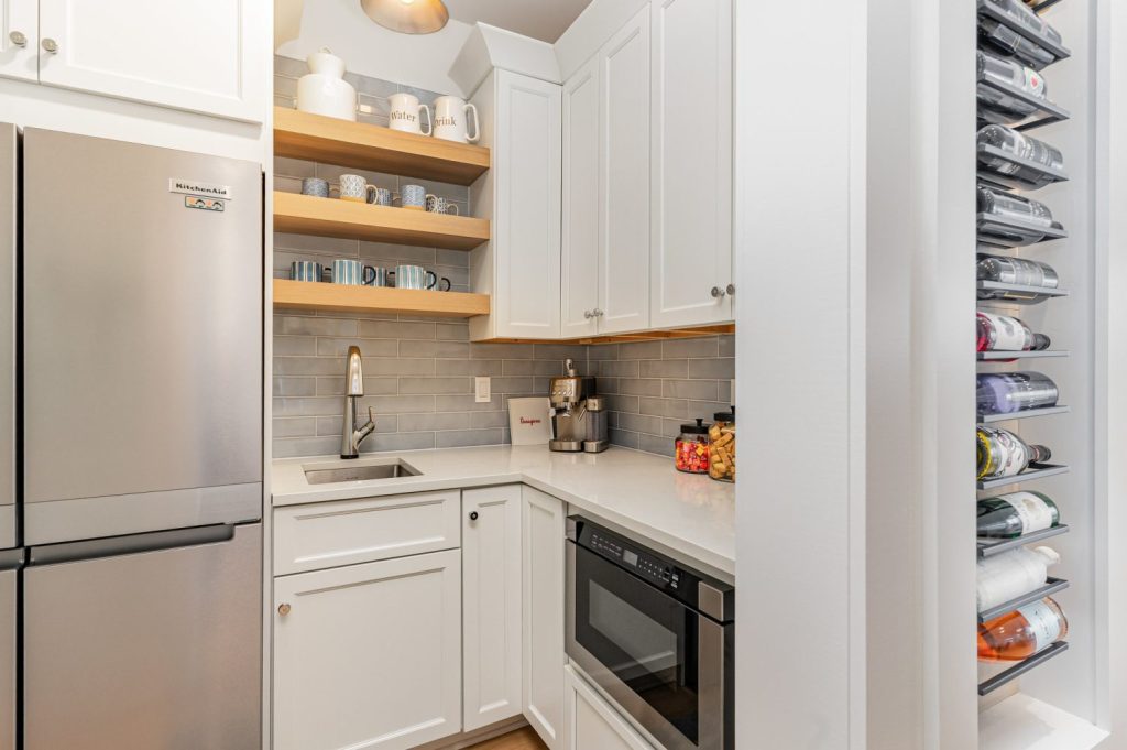 Angle view of kitchen island with Atlas Homewares Everitt Collection polished chrome cabinet hardware paired with quartz countertops. Scullery and butters pantry with knobs