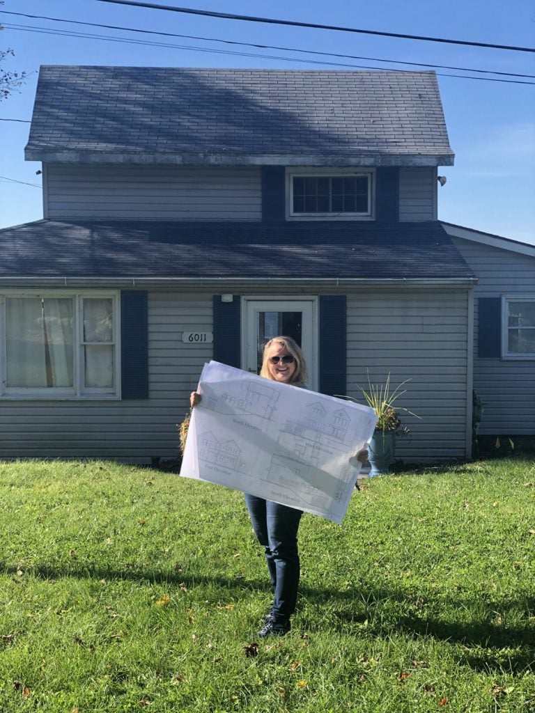 Amie Freling holding renovation blueprint in front of the cottage on Cayuga Lake