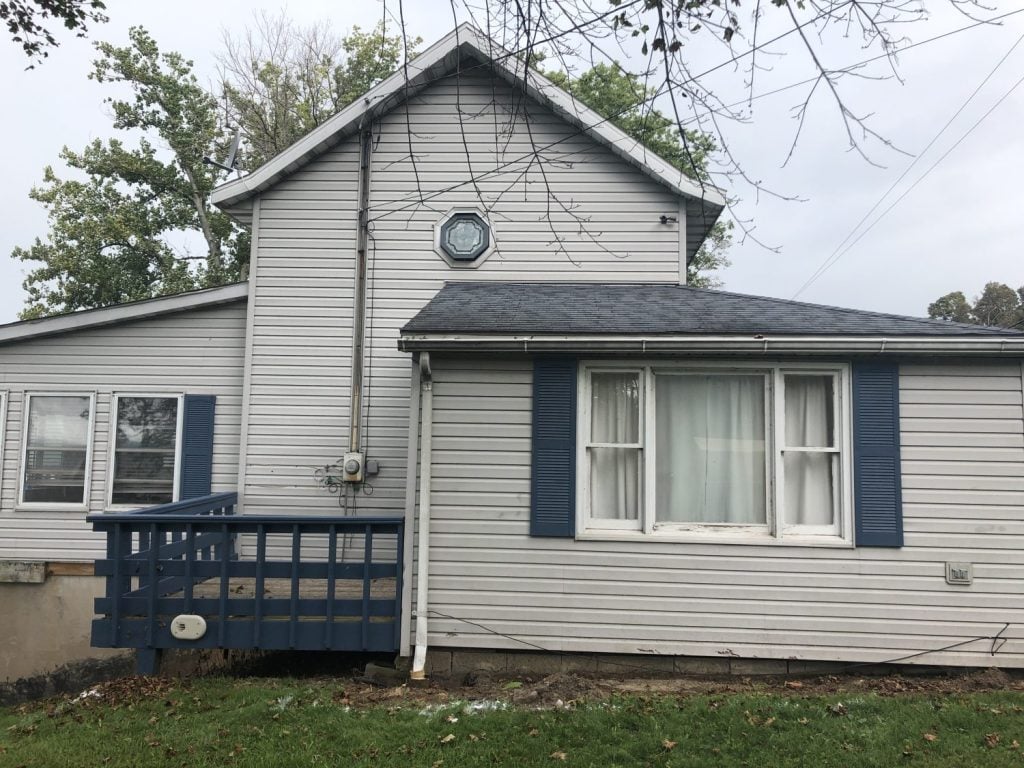 The side of the cottage with a blue wood deck and white windows that are old 