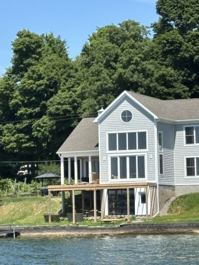 the lake side view of a new construction home being built on Cayuga Lake . there is gray shake siding and a round window 