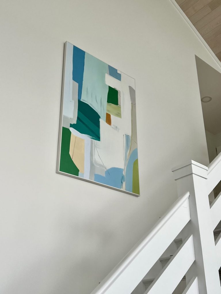 Affordable hand-painted art from Vinchy Art displayed above a white staircase, featuring a large abstract painting in blue, green, and beige tones.