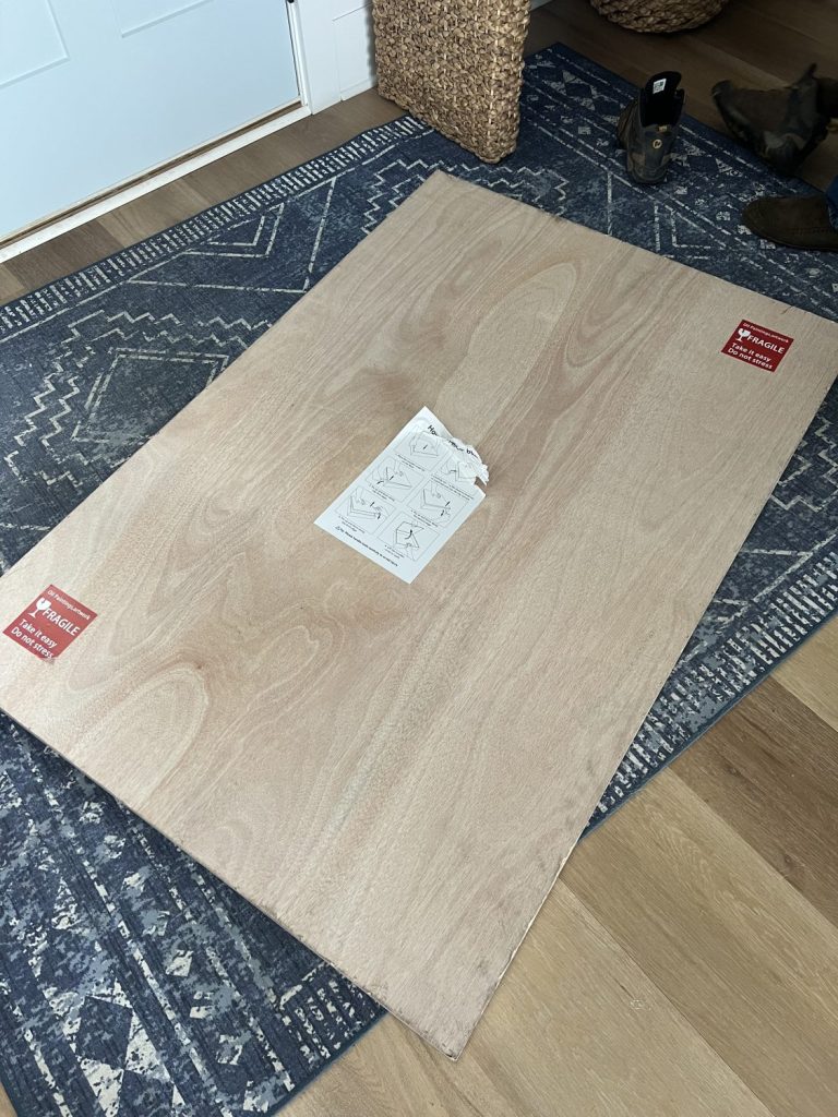 Solid wood shipping box from Vinchy Art placed on a blue patterned rug, showing protective packaging with fragile stickers and instructions on top.