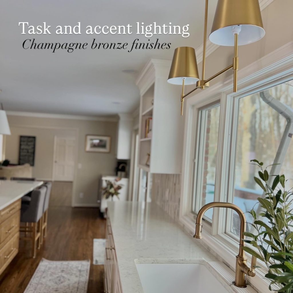 Luxury kitchen remodel featuring champagne bronze task and accent lighting, brass wall sconces over an enlarged picture window, quartz countertops, white shaker cabinets, farmhouse sink, and designer brass faucet in a bright open-concept kitchen renovation.