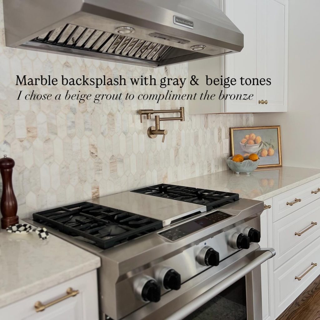 Luxury kitchen remodel featuring a marble tile backsplash with warm gray and beige tones, professional stainless steel gas range and vent hood, pot filler faucet in champagne bronze, white shaker cabinets, and quartz countertops in a custom designer kitchen renovation.